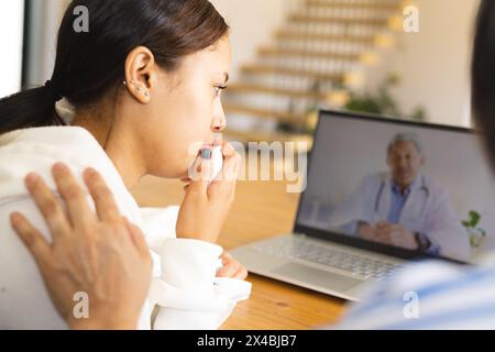 La grand-mère asiatique réconforte l'enfant biracial sur l'appel vidéo à la maison, à la fois en regardant l'ordinateur portable. Grand-mère aux cheveux courts, petite-fille montrant une longue ha brun Banque D'Images
