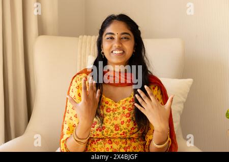 Femme indienne dans une tenue vibrante rit pendant un appel vidéo à la maison. Ayant de longs cheveux noirs et des yeux sombres, profitant d'un moment de joie dans sa tenue vibrante, Banque D'Images