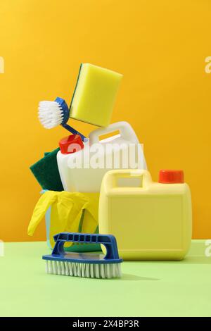 Idée créative pour la publicité des produits détergents. Bidons en plastique blanc et jaune avec brosses, éponges et gants en caoutchouc décorés sur dos jaune Banque D'Images