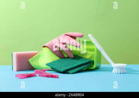 Scène publicitaire pour produit de nettoyage. Idées créatives avec panier en plastique rempli d'essuie-glace, éponges, brosse et pince à linge décorés sur un dos vert Banque D'Images