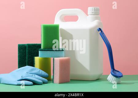 Sur fond rose, boîte en plastique blanc décorée d'éponges colorées, de gants en caoutchouc et d'une brosse. Maquette d'étiquette vierge de bouteille de détergent pour Banque D'Images