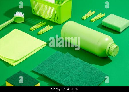 Produits de nettoyage verts sur un fond vert Uni. Bouteille de détergent non étiquetée, chiffon, brosse et éponges décorés. Concept de nettoyage de maison, scène pour un Banque D'Images