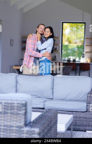 Couple diversifié embrassant dans une maison confortable, souriant chaleureusement, espace de copie. Il a les cheveux bruns courts, elle a de longs cheveux noirs et la peau brun clair, inaltérée Banque D'Images