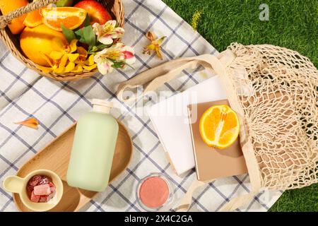 Panier de pique-nique avec des fruits et des fleurs décorés avec des livres de conteneur de sac en maille, boîte à blush et confitures sur tissu à carreaux. Un flacon vide s'affiche sur BT Banque D'Images