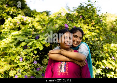 Mère indienne et fille adolescente embrassant, les deux souriants dans le jardin, espace copie. Mère aux cheveux noirs, fille adolescente aux yeux bruns, portant du bleu Banque D'Images
