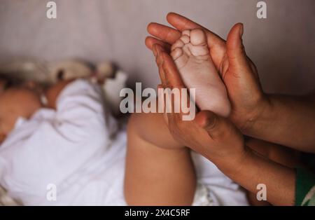 Image en gros plan montrant une mère tenant tendrement le pied de son bébé dans ses mains, symbolisant les soins et la protection. Banque D'Images