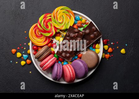 Divers bonbons colorés, sucettes et macarons. Plat étendu sur fond de pierre Banque D'Images