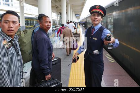 (240502) -- URUMQI, 2 mai 2024 (Xinhua) -- Airkir Duliki (R) aide les passagers à monter à bord d'un train de Chengdu à Kashgar à une gare de Chengdu, dans la province du Sichuan, au sud-ouest de la Chine, le 20 avril 2024. Airkir Duliki, le chef de train tadjik âgé de 27 ans, est né et a grandi au milieu des montagnes enneigées et des prairies dans un village du comté autonome tadjik de Taxkorgan sur le plateau du Pamir, où les chemins de fer n'étaient pas courants pour les résidents dans le passé. La première expérience d'Airkir avec le voyage en train s'est produite quand elle s'est rendue à Urumqi pour l'université au Xinjiang. Accompagné de son père Banque D'Images