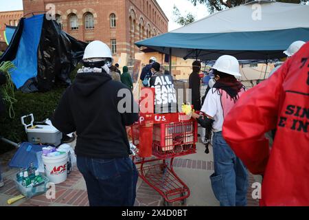 Los Angeles, Californie, États-Unis 1er mai 2024. TOUS LES MOYENS NÉCESSAIRES» écrit sur un seau à ordures transporté dans un chariot rouge et poussé par des manifestants dans des casques et des masques à gaz. Université de Californie, Los Angeles (UCLA) le 1er mai 2024 : manifestants pro-Palestine/Hamas dans leur campement de tentes : ils ont construit des murs autour de lui avec du contreplaqué et refusent l'entrée des étudiants juifs et des journalistes. May qualifie l'attaque du 7 octobre du Hamas contre Israël de "Fake News" et la protestation semble plus sur l'appel à la chute des gouvernements occidentaux et à l'éradication d'Israël, ce qu'ils nient avoir fait Banque D'Images