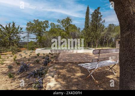 Banc en bois blanc style vent sous un chêne ombragé à côté d'une jolie piscine extérieure carrelée de verdure avec vue magnifique sur la campagne et bri en terre cuite Banque D'Images