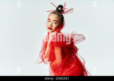 Femme asiatique frappant pose dans une superbe robe rouge et voile assorti. Banque D'Images
