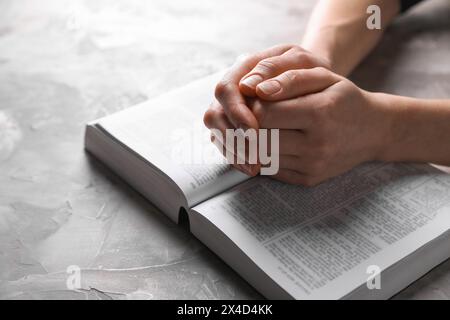 Religion. Femme chrétienne priant sur la Bible à la table texturée grise, gros plan Banque D'Images