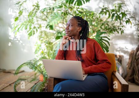 Réfléchie femme noire détendue prendre une pause du travail sur ordinateur portable regarder côté fenêtre, verdure maison. Banque D'Images