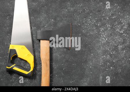 Scie avec poignée jaune et hache sur fond texturé gris foncé, pose à plat. Espace pour le texte Banque D'Images