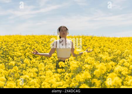 femme méditant et pratiquant le yoga dans une prairie pleine de fleurs jaunes colorées. Relaxation spirituelle dans la nature Banque D'Images