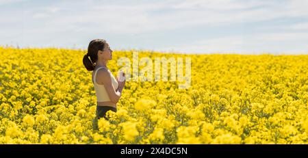 Femme respirant l'air frais dans un champ jaune et pratiquant la méditation yoga Banque D'Images