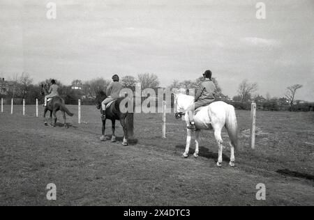 Années 1960, historique, dans une école d'équitation de banlieue, trois filles à cheval au bord d'un champ, Angleterre, Royaume-Uni. Banque D'Images