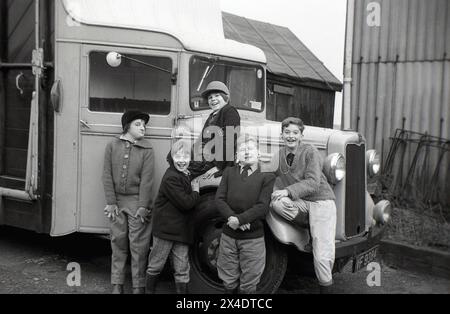 Années 1960, historique, les écoliers s'amusant sur la roue de boite à cheval ou camion à cheval de l'époque, posant pour une photo à l'extérieur dans la cour d'une école d'équitation de banlieue, Angleterre, Royaume-Uni. Banque D'Images