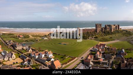CHÂTEAU DE BAMBURGH, NORTHUMBERLAND, ROYAUME-UNI - 23 AVRIL 2024. Vue panoramique de paysage aérien du château de Bamburgh et terrain de cricket du village qui est un populaire Banque D'Images