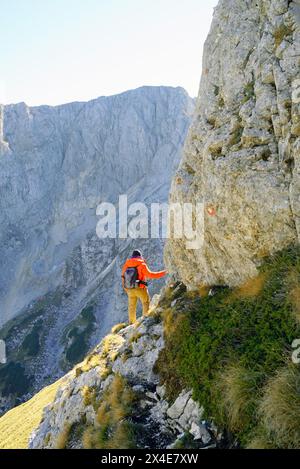 Un touriste vêtu d'une veste brillante s'est arrêté à une falaise de montagne. Photo du dos d'un homme engagé dans des loisirs actifs - randonnée à Durmitor, Monténégro Banque D'Images