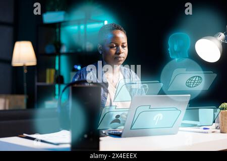 Femme afro-américaine utilisant un ordinateur portable, interagissant avec l'assistant d'intelligence artificielle en utilisant la technologie AR. Personne du BIPOC travaillant avec la technologie AR, donnant des commandes au compagnon virtuel de l'IA Banque D'Images