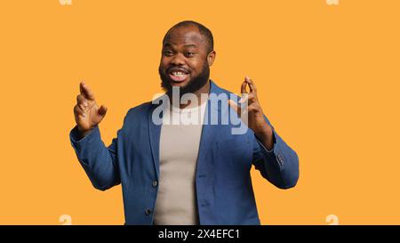 Portrait d'homme afro-américain optimiste croisant les doigts, faisant du vœu, isolé sur fond jaune de studio. Jolly BIPOC personne espérant bonne chance, attendant le miracle, caméra A. Banque D'Images