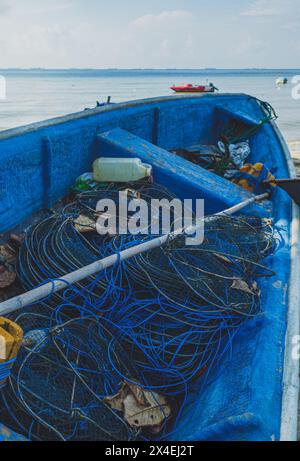 Un bateau de pêche en bois bleu vif rempli de filets de pêche repose sur une plage de sable. Banque D'Images