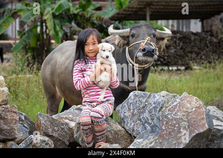 Jeune fille dans le Vietnam rural tenant un chien à côté d'un buffle d'eau dans la province de Lao Cai, Vietnam Banque D'Images