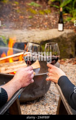 États-Unis, État de Washington, Woodinville. Un homme et une femme dégustent un verre de vin rouge devant un feu de camp. Banque D'Images