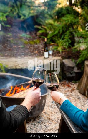 États-Unis, État de Washington, Woodinville. Un homme et une femme dégustent un verre de vin rouge devant un feu de camp. Banque D'Images