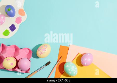 Oeufs de Pâques peints à la main décorés sur un fond bleu clair avec pinceau et cartes en papier. Vue de dessus, espace pour la conception. Concept de célébration de Pâques Banque D'Images