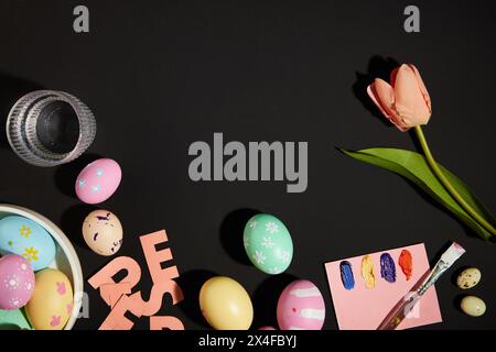 La décoration des oeufs pour Pâques.​ oeufs colorés, pinceau et fleur décorés sur fond noir. Vue de dessus, espace vide pour la conception Banque D'Images