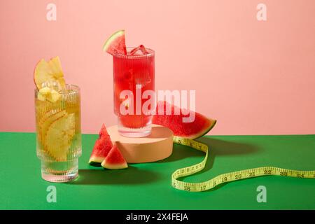 Vue de face de deux tasses de jus de pastèque et de pomme décorées avec des tranches de pastèque fraîches et ruban à mesurer sur un fond rose. La pastèque a de l'alwa Banque D'Images