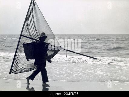 Pêcheur de crevettes avec son filet et son panier sur la plage, 1923. Banque D'Images