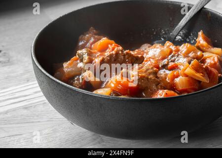 Casserole de bœuf, avec herbes et légumes, dans un vin rouge et sauce tomate. Dans un bol en grès noir. Banque D'Images