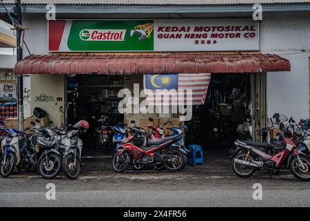 Un atelier de réparation de motos traditionnel en Malaisie, rempli de différents modèles de motos et de scooters sous un signe Castrol de marque. Le drapeau malaisien Banque D'Images