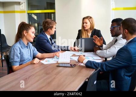 Une femme PDG dirige les réunions d'affaires dans une salle de réunion moderne. Les cadres multiethniques s'engagent dans des discussions d'équipe avec un ordinateur portable, des graphiques, des diagrammes. Pro multiracial Banque D'Images