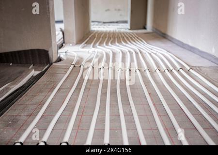 Vue en angle bas sur les tubes blancs minces courbés dans la courbe complexe du nouveau collecteur de système de distribution en laiton monté pour le plancher de chauffage central dans une résidence Banque D'Images