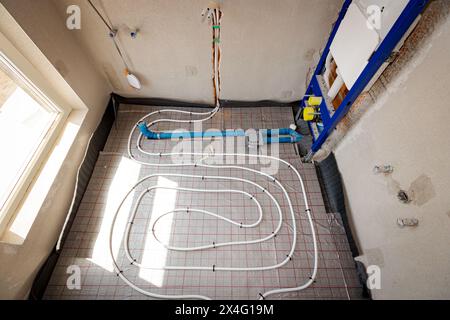 Les tubes blancs minces sont pliés dans la courbe complexe du nouveau laiton, collecteur de système de distribution monté pour le plancher de chauffage central dans la salle de bains inachevée, resi Banque D'Images