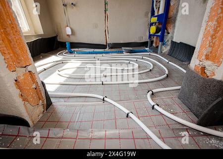 Les tubes blancs minces sont pliés dans la courbe complexe du nouveau laiton, collecteur de système de distribution monté pour le plancher de chauffage central dans la salle de bains inachevée, resi Banque D'Images