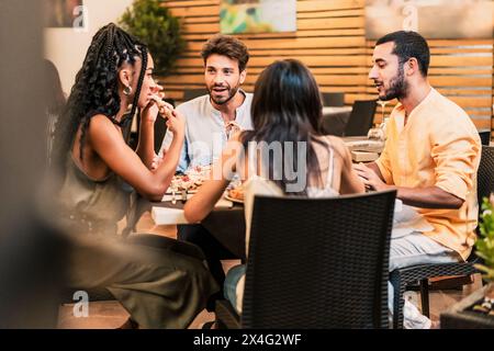 Groupe diversifié d'amis - profiter du dîner et de la conversation dans un restaurant, partager un repas dans un cadre urbain animé - social, amusant. Banque D'Images