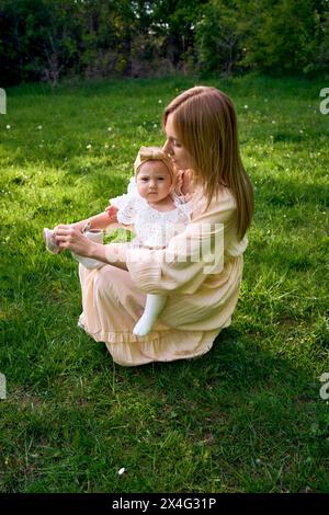 mère met des chaussures sur sa petite fille dans le parc Banque D'Images