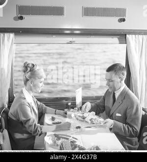 Voyage en train dans les années 1960 Un couple dans la voiture-restaurant du train profite du dîner ensemble. Elle a une coiffure typique des années 1960. 1964 Kristoffersson réf. DD107-8 Banque D'Images