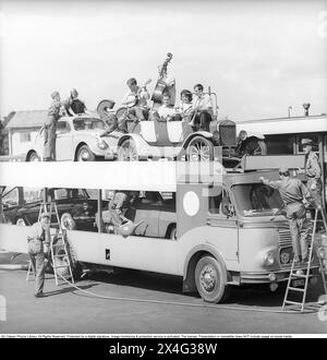 Personnel de la station-service Esso rétro. Une image amusante des années 1960 quand un groupe d'hommes dans les vêtements de l'entreprise est vu donnant service à un camion transportant des voitures de différents modèles, y compris une voiture vétéran avec un groupe avec leurs instruments. Photo prise lors du tournage d'une publicité ou d'une publicité. La société Svenska Esso était une marque suédoise entre les années 1939 et 1987, lorsque les stations ont changé leur nom pour le nom du nouveau propriétaire Statoil, et est maintenant la marque Circle K. Suède 1963. Kristoffersson réf. DC98-4 Banque D'Images