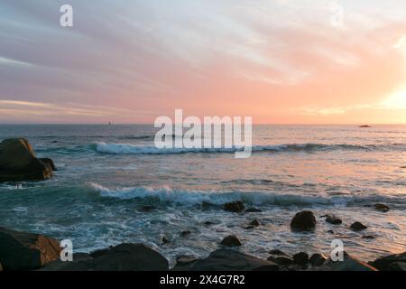 Coucher de soleil peint la mer et les rochers dans des tons chauds et tranquilles Banque D'Images