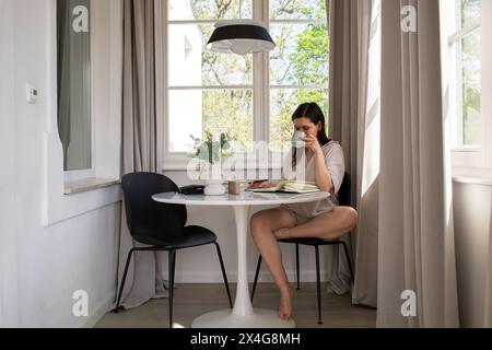 Jeune femme assise à table, écrivant dans un journal et buvant du café Banque D'Images