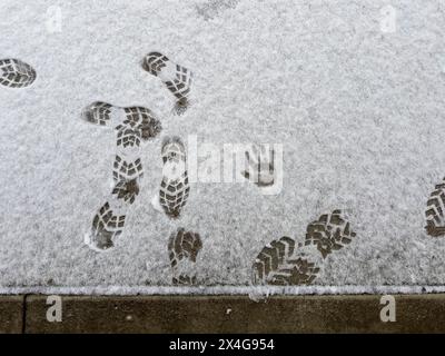 Empreintes de pieds et petite empreinte de main dans la neige fraîche sur béton Banque D'Images