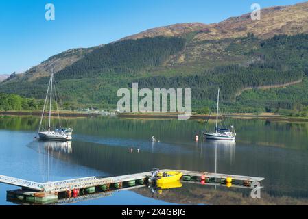 En regardant vers le nord au-dessus du Loch Leven à l'A82 au village de Ballachulish. Bateaux aux couleurs vives amarrés sur le loch. Réflexions. Près de Fort William, , Écosse, Royaume-Uni Banque D'Images