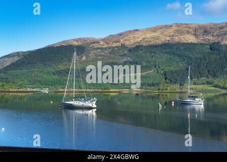 En regardant vers le nord au-dessus du Loch Leven à l'A82 au village de Ballachulish. Bateaux aux couleurs vives amarrés sur le loch. Réflexions. Près de Fort William, , Écosse, Royaume-Uni Banque D'Images