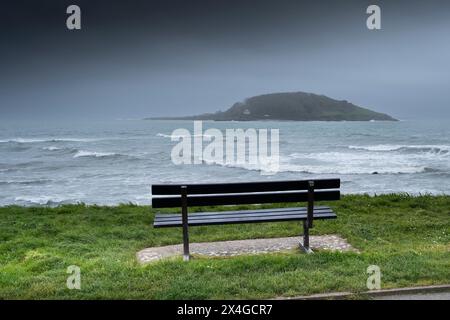 Météo britannique. Un banc surplombant la mer et l'île historique Looe au large de la côte de Cornouailles au Royaume-Uni. Banque D'Images